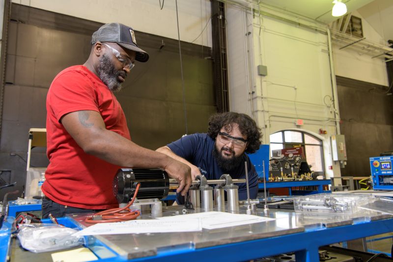 Two students wearing safety goggles working together on mechanical equipment. 