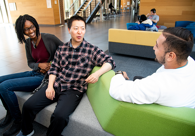 three racially diverse students speaking on student union couch