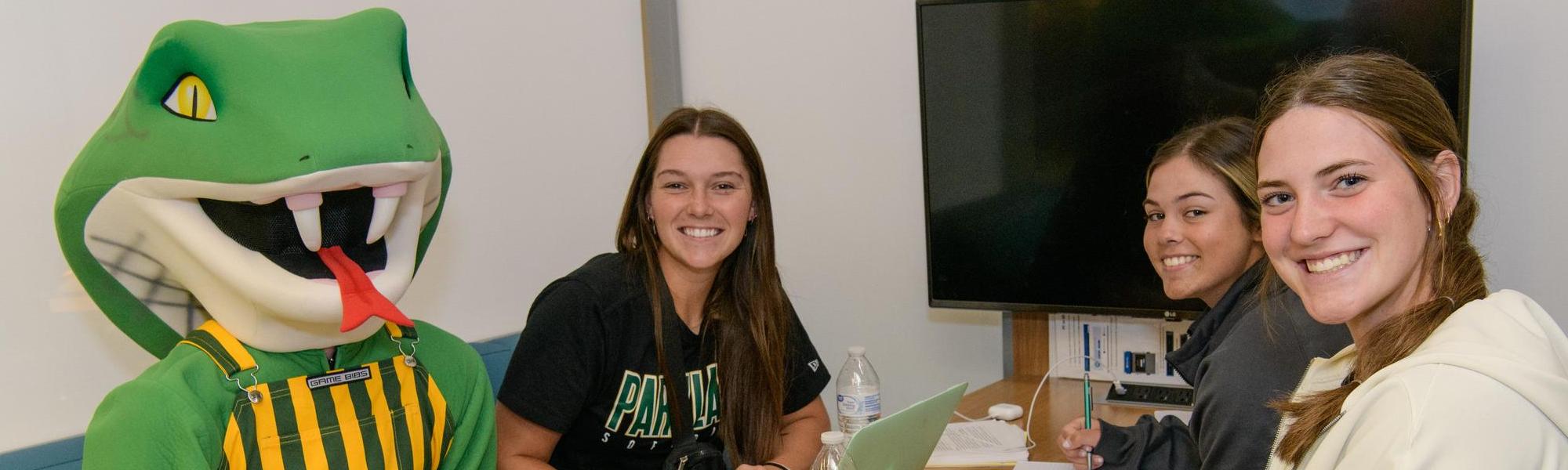 Three female students smiling with Cobra mascot in Library