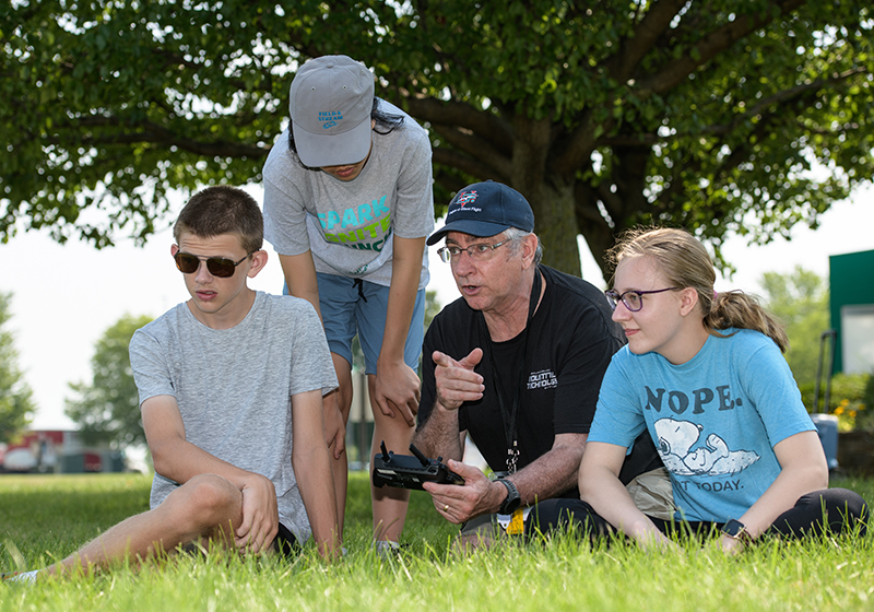 three students outside with instructor, holding controller for drone